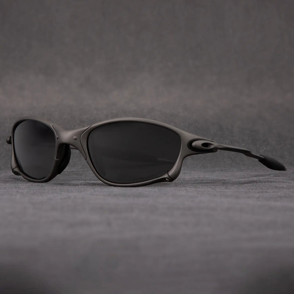 A pair of black, oval-shaped polarized sunglasses with a sleek, matte frame is displayed on a gray surface against a gray background, offering stylish outdoor eyewear with UV protection.